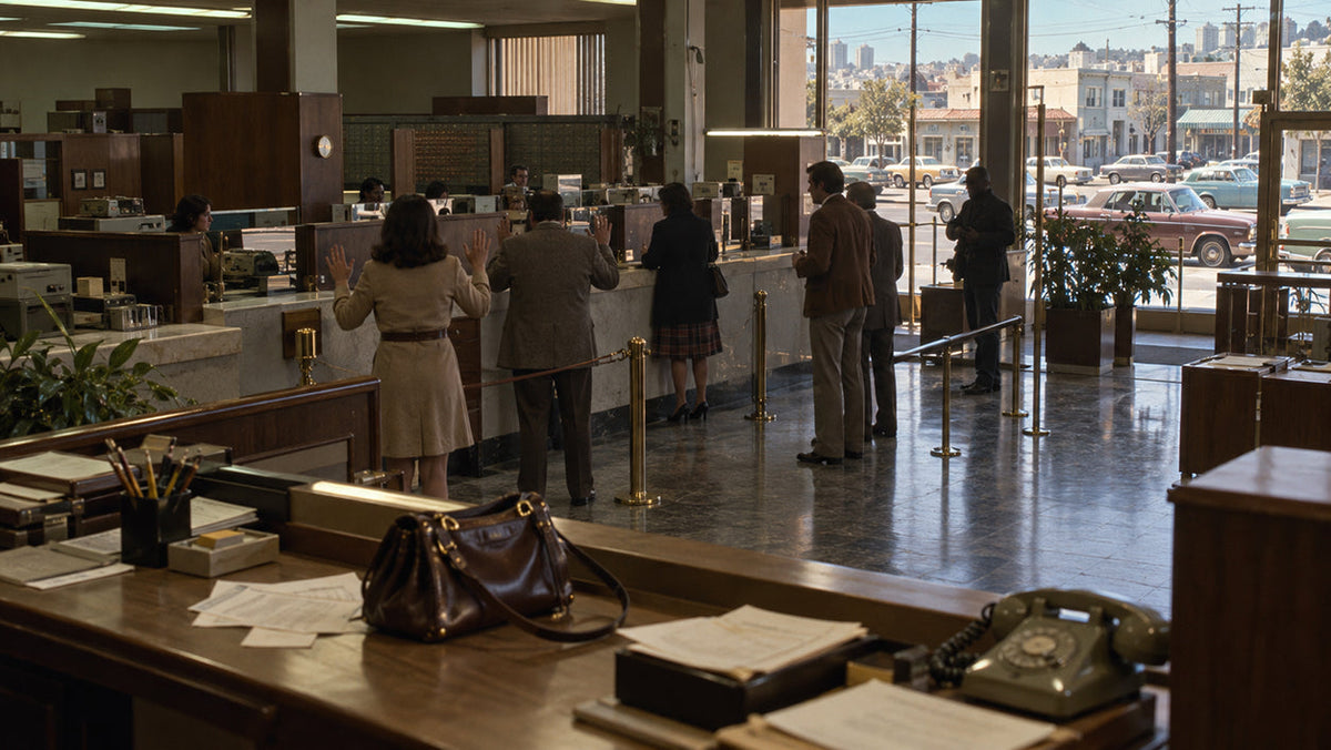 A tense reconstruction of a 1974 San Francisco bank interior with period security-camera equipment, deserted counters and daylight falling across the floor.